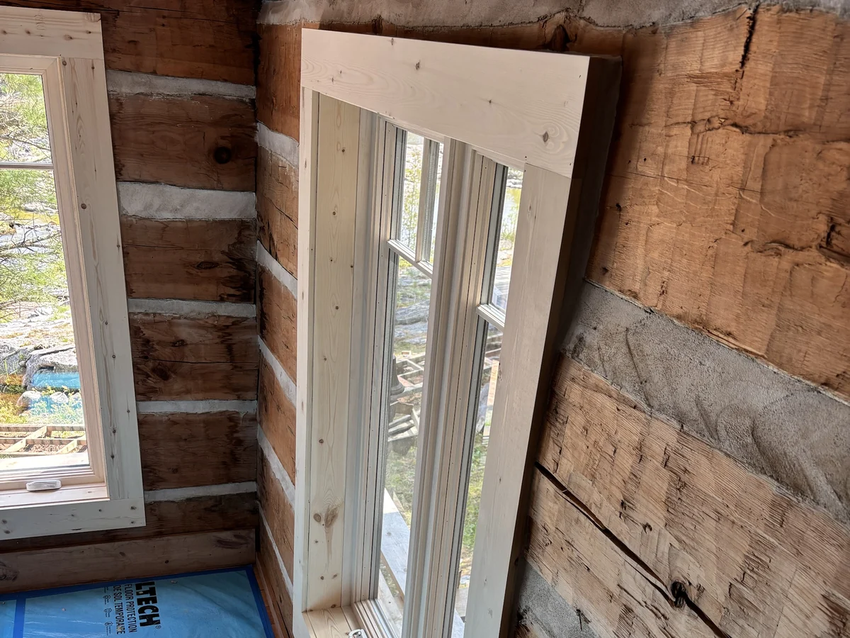 Wide pine window casing and sill fitted to a hand-hewn log wall